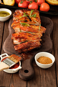 牛肉猪熏制美味的烧烤肋骨配上辣酱汁用切碎的新鲜蔬菜在老生锈的木制砍板上供餐图片