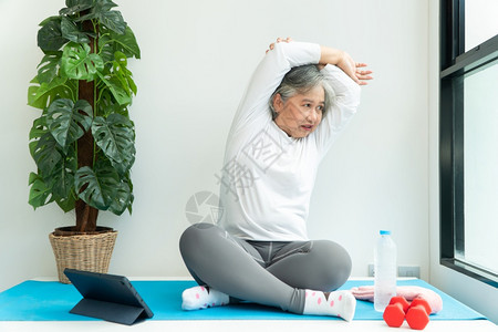 理疗健身房女上笔记本电脑在线课程的亚洲老年妇女在家中起居室练习时观看膝上型计算机在线课程网上锻炼培训概念图片