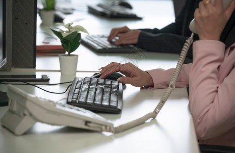 妇女在办公桌计算机工作时通过电话交谈在办公室工作场所从事繁忙工作的概念在办公室工作场所从事繁重工作女座机商业图片