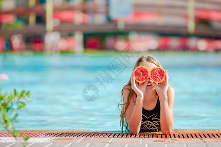 脸肖像美丽的小女孩用橘子遮眼睛在游泳池上被孤立的橙子遮眼睛在背景游泳池旁的眼里被柳橙子蒙睛图片