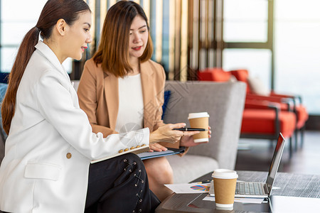 曼谷常设两名与伙伴企业合作的亚裔女企业家将笔指向现代办公室或合用空间的技术膝上型电脑咖啡室休息伴侣和同事讨论集思广益概念商业图片