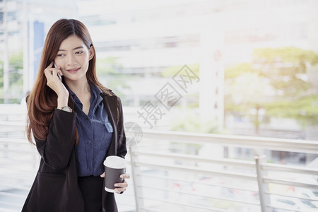 女士商人使用手机和微笑的面部电话进行商业交易职女工穿黑色西装手持智能电话谈论无线移动技术概念工作妇女穿黑色西装外部年轻的图片