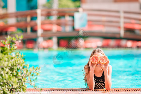 食物水果快乐的小女孩用红橙子遮着眼睛伪装成游泳池的背景女孩用橘子眉眼在背景游泳池旁的眼皮上涂橙子脸吃图片