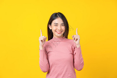 亚洲微笑的年轻女子指向广告横旗或以孤立的黄色背景展示身着冬季舒适的毛衣室内工作快乐与趣复制空间概念Namei时髦的尚吸引人图片