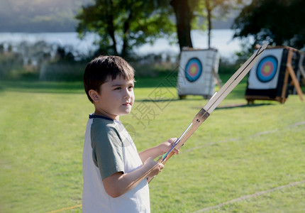 T恤孩子在夏营探险中户外活动的混合种族儿童在体育学校的训练中与箭弓交火的男孩射和箭击参加运动学校的训练目标图片