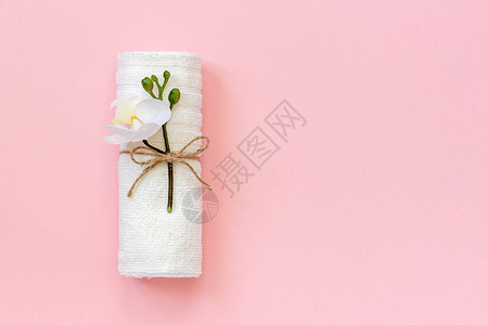 卫生浴室白色毛巾卷用绳子绑在粉色纸背景上带有兰花小枝复制空间模板用于刻字文本或您的设计用绳子绑在粉色纸背景上的白毛巾卷复制空间模图片