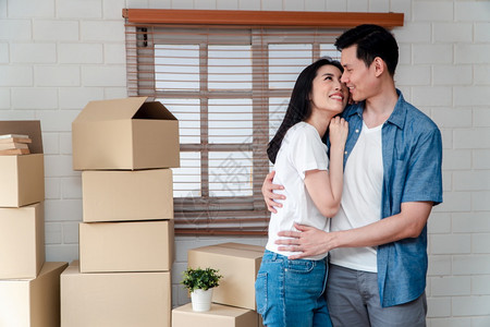 坐着买下新婚夫妇开始生活的概念在购买新家后搬来的路上用纸板盒拥抱男友时使用纸板盒拥抱着男朋友的年轻亚洲快乐情侣微笑财产人们图片