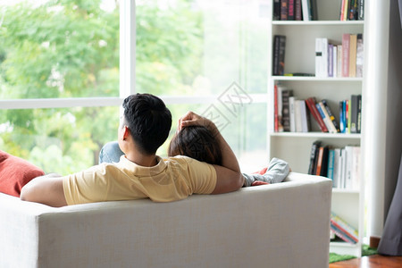 坐在沙发上快乐的一对情幸福侣作为一个男人在客厅里爱着自己的女友并且放松一下情人节浪漫的概念求婚和姻吻随意的亚洲图片
