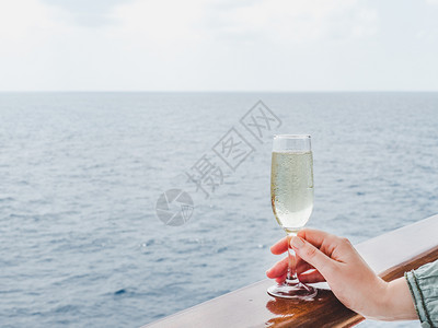 在蓝海浪背景下游轮露天甲板上举着美丽玻璃的时装妇女侧观特近休闲和旅行概念女在甲板上举着玻璃女士在甲板上举杯鸡尾酒日落人们图片