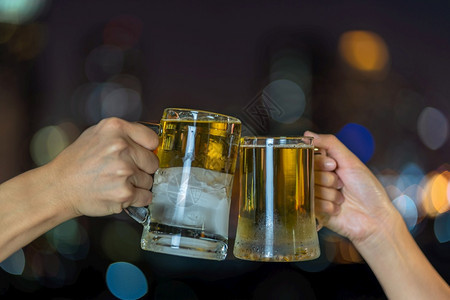 为了金子清爽手握与两个啤酒杯或子连在一起城市景色模糊的相片上欢庆狂和祝新年概念图片