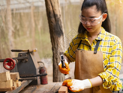 妇女站立建筑工身着经检查的衬衫在建筑工地作在木板上钉内部的木制头图片