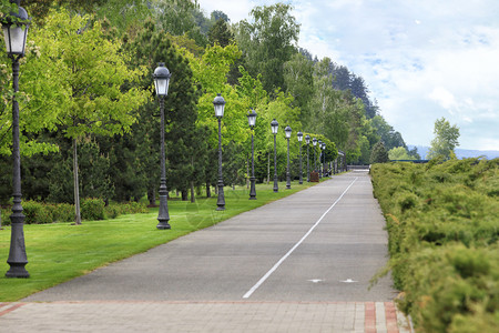 老的一条笔直柏油路和一条自行车道沿着美丽的修剪过绿色草坪穿一个夏季公园路边有许多漂亮的旧灯笔直柏油路和自行车道穿过公园有许多美丽图片