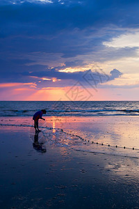 一位亚洲女利用黄昏海滩上的渔网捕食咸水鱼在泰国南部背景的日落天空中飞速升起盐水景观蓝色的图片