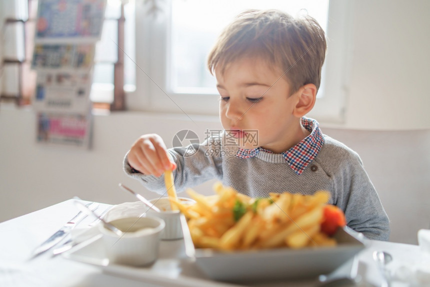 手小可爱的caucasiansian小男孩的肖像他吃薯条片在餐厅的桌上或在家中三四岁坐在桌边白天子旁边可口儿图片