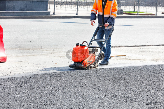 夯公路工人用汽油振动式压机铺有汽油振动式压机的沥青在道路修理工点使用电动板压缩沥青路面人行道图片