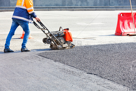 工路服务人使用电动板压紧在道路修理工点压缩沥青公路工人用含汽油振动机的沥青街道械器图片