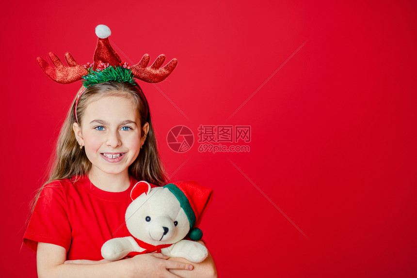 一个有趣的快乐女孩肖像头上缠着角绷带抱一只泰迪熊穿着圣诞睡衣背景为鲜红色头抱着一只泰迪熊与鲜红色背景隔开指数假期自信的图片