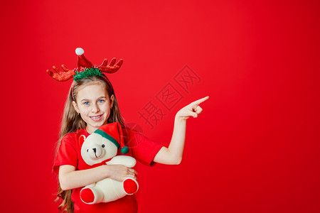 一个有趣的快乐女孩肖像头上缠着角绷带抱一只泰迪熊穿着圣诞睡衣背景为鲜红色头抱着一只泰迪熊与鲜红色背景隔开鹿手广告图片