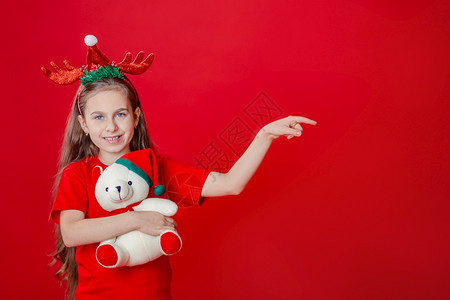 美丽的快乐拥抱一个有趣快乐女孩肖像头上缠着角绷带抱一只泰迪熊穿着圣诞睡衣背景为鲜红色头抱着一只泰迪熊与鲜红色背景隔开图片