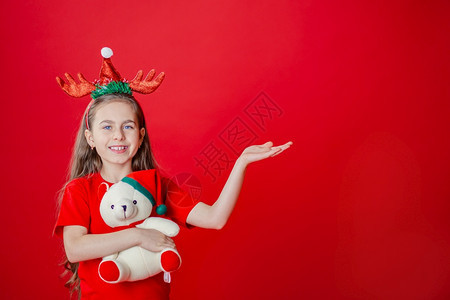 一个有趣的快乐女孩肖像头上缠着角绷带抱一只泰迪熊穿着圣诞睡衣背景为鲜红色头抱着一只泰迪熊与鲜红色背景隔开手势年轻的微笑图片