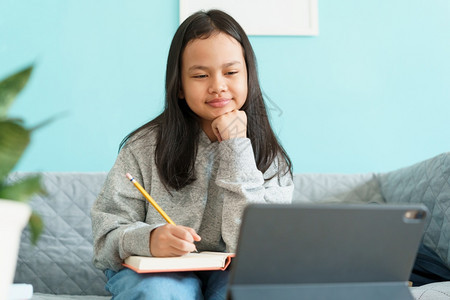 坐着亚裔儿童在家中客厅坐沙发上旁听亚洲儿童观看并写作业或练习家庭在线学概念校对Portnoyunorg孩子们聪明的图片