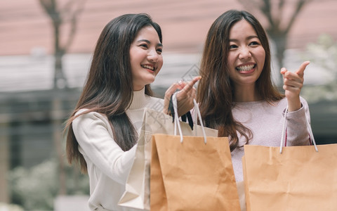 冬天亚洲人两个美丽的亚洲妇女笑着快乐拿纸袋和做窗户购物冬季友谊和销售折扣概念笑声iBARBAR指点图片