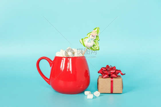 有创造力的红色杯棉花糖与绿棒圣诞树和蓝色背景礼品盒圣诞快乐或新年概念复制空间模板为您的设计贺卡红色杯棉花糖与绿棒圣诞树和蓝色背景图片