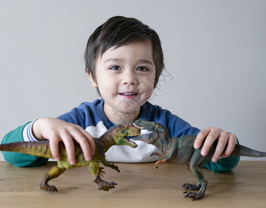 嘴头发在家木桌边玩恐龙具的活生小男孩快乐子与他两只恐龙一起玩乐为他的放松时光而奋斗孩子的发展和想象概念儿童发展和想象力相机图片