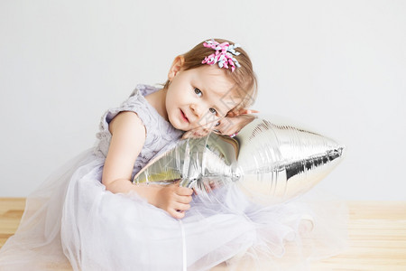 纯真游戏优雅的一个穿着灰色礼服的可爱小女孩肖像站在白色背景面前的小公主女儿玩银星形气球的小宝女孩图片