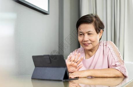 泰国数字的尽管快乐微笑亚洲高龄女在隔绝和家与人隔离时在数字平板电脑上播放视频话穿着粉红色衣服的老年妇女通过互联网技术与人们交谈时图片