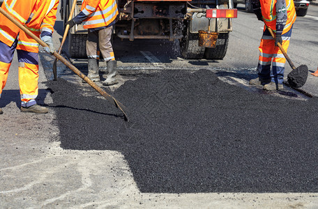 道路工人作组以新鲜热沥青来更部分公路并平滑其修补工作组在修复公路时手工用铲子擦干热沥青用铲子粉刷热沥青建造为了劳动图片