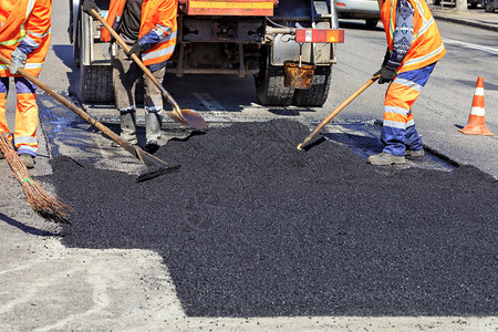 碎石乌克兰热的道路工人作组以新鲜热沥青来更部分公路并平滑其修补工作组在修复公路时手工用铲子擦干热沥青用铲子粉刷热沥青图片