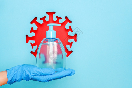 安全手套中的拿着针对抽象红色冠状细菌微生物蓝色背景的消毒剂防腐或抗菌皂的药房蓝色背景创意概念卫生保健瓶子产品图片
