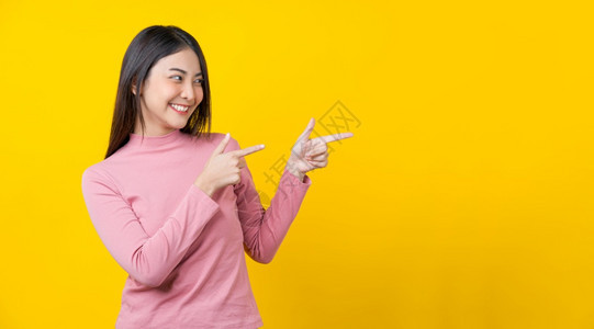 女孩亚洲微笑的年轻女指广告横旗或以孤立的黄色背景展示身穿冬季舒适的毛衣室内工作幸福和乐趣复制空间概念笑容和娱乐赞同愉快图片