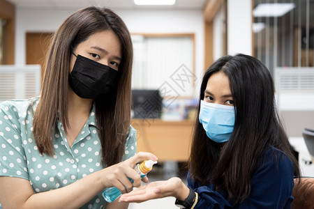 戴口罩的女性手拿消毒酒精给对方消毒图片