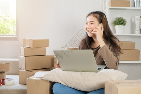 包裹顾客快乐的亚洲年轻企业家在智能手机上与客户交谈以获得大货订单她为在家办公室的销售成功微笑在线商户业务和电子的概念女士背景图片