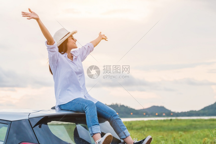 亚洲人冒险快乐的亚洲女在日落下海边的汽车屋顶上散布在度假旅行期间带着自然背景与在海边充满阳光黎明和山地度假概念的欢乐女孩士图片