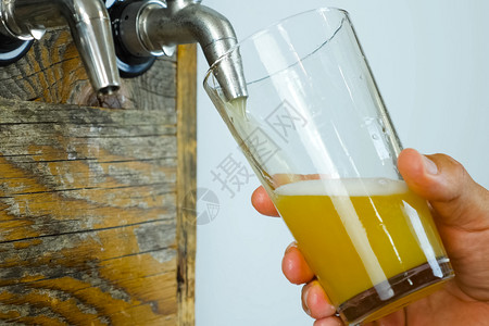 调酒师从吧的水龙头将啤酒倒入玻璃杯啤酒装瓶从吧的水龙头将啤酒倒入玻璃杯啤酒装瓶木头浇注图片