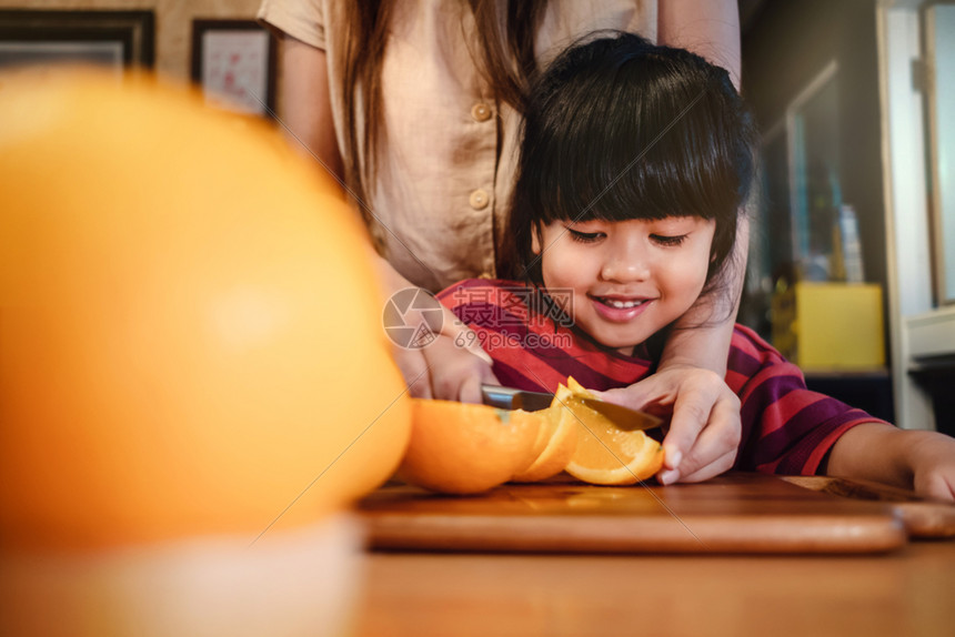 刀幸福夏天快乐的可爱34岁年老女孩与她的妈切除一些橙子在木质餐桌上食品室的青春女孩正在学习烹饪她的母亲水果和蔬菜的孩子概念图片