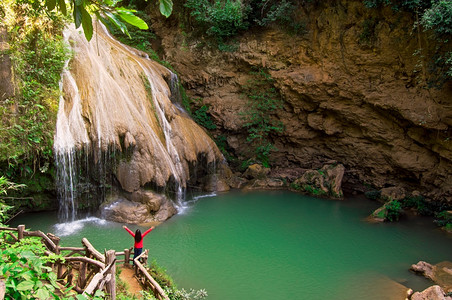 一个穿红衬衫的女人正在欣赏一个绿色瀑布的美景在森林和山丘中间美丽的自然高卢昂瀑布林丰光露江瀑布水河热带图片