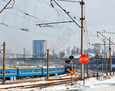 象征等待乌克兰铁路道口的红色停车标志以铁轨蓝色火车厢和冬季城市入口处的景观为背铁路道口的红色停车标志以火站和冬季城市的建筑物为背图片