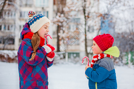 蜜糖一个女孩和男在冬天的街道上手里拿着圣诞糖果的肖像兄弟姐妹在假期里玩得很开心在冬天的街道上一个女孩和男手里拿着圣诞糖果的肖像印背景图片