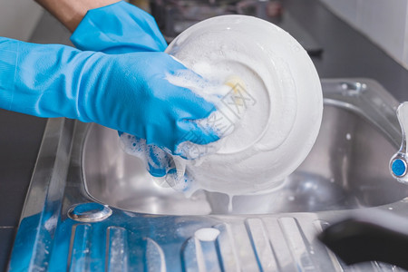 海绵工作洗涤剂一个穿着蓝色橡胶手套的近身男子在厨房水槽里用洗碗液杯子他当时正戴着一个蓝色橡胶手套图片