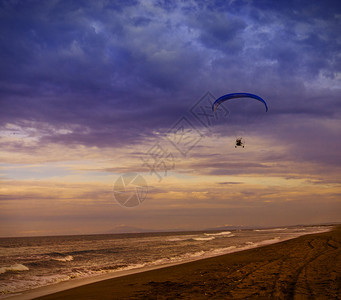 云自然动力滑翔伞飞过海面向日落天空飞越的行图片
