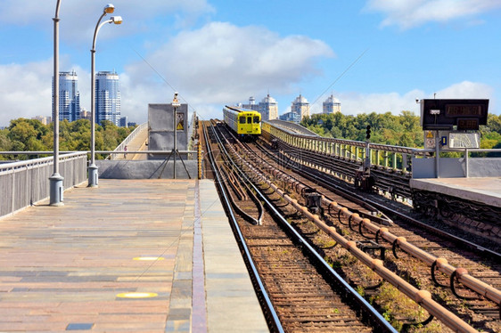 基辅一座地铁桥路轨迹的开阔部分在城市风景的背下一辆柠檬色地铁列车沿这条路横行而蓝色的天空前方则略微模糊供复制空间使用地铁列车穿过图片
