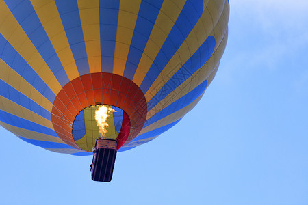 火焰的将空气用黄蓝色闪亮的美丽气球加热并将一篮游客举到蓝天上从下方向飞去在蓝天空中紧贴一个美丽的气球飞行运动颜色图片