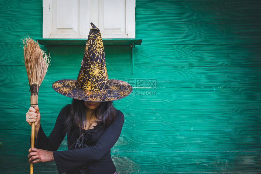 万圣节艺术设计美丽的年轻女孩戴着巫帽子和扫帚在她手中绿色墙背景白种人女士派对图片