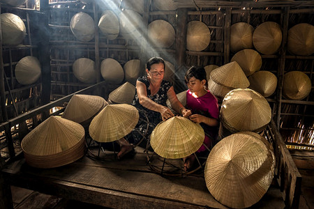 行业女士越南老工匠在霍希明市ApThoiPhuoc村的老旧传统房屋中教孙辈制作传统的Vietnam帽子传统艺术家概念抽烟图片