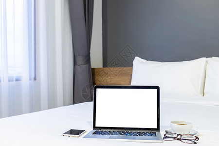 技术在旅馆卧室内背景工作和业余度假期旅行时带空白屏幕的手提式电脑智能手机咖啡杯和眼镜贴在白色床上装饰的品上家当代的图片