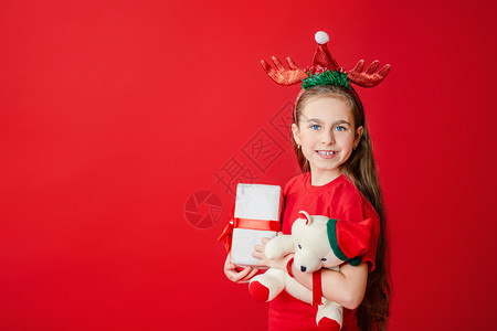 白种人孩子一个有趣的快乐女孩肖像头上缠着角绷带抱一只泰迪熊穿着圣诞睡衣背景为鲜红色头抱着一只泰迪熊与鲜红色背景隔开假期图片